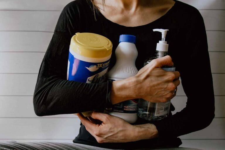A woman holding a bunch of cleaning supplies with two arms to her body to help illustrate DIY vs Professional Cleaning and What Is Spring Cleaning