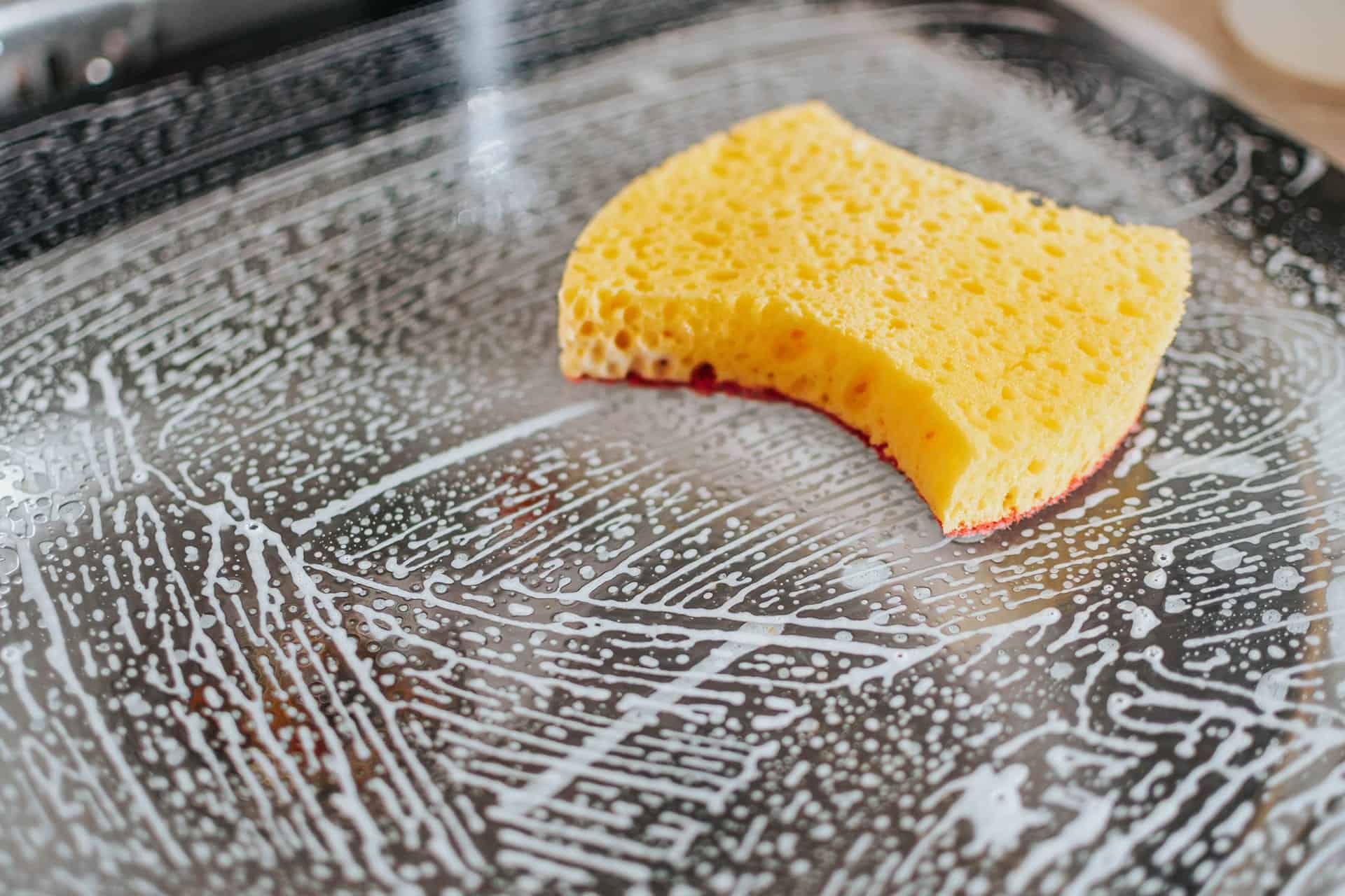 Image of a big yellow sponge on a soapy dark countertop  to help illustrate what is Spring cleaning.