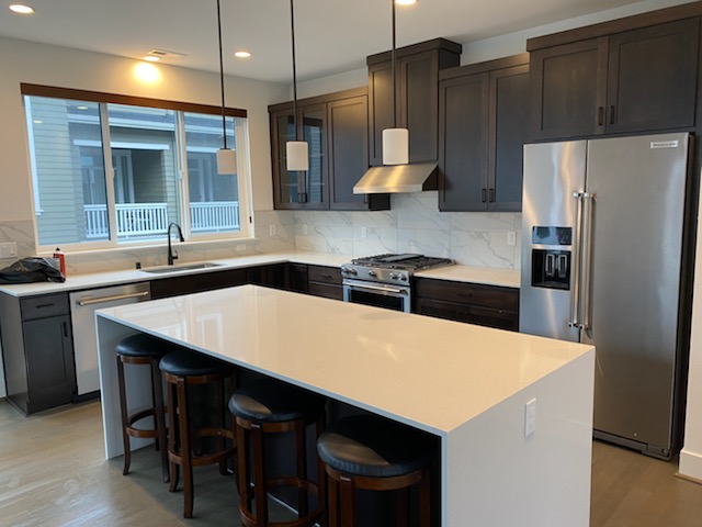 Modern kitchen with dark cabinetry, white countertops, pendant lighting, and stainless steel appliances