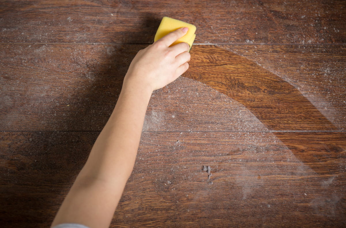 Someone cleaning off a dusty table with a sponge to help illustrate Summer House Cleaning Checklist